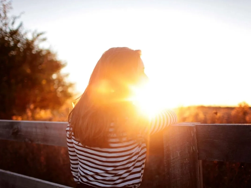 Uma mulher aproveitando o sol do final da tarde em um campo, representando como a luz solar é a principal forma de obter vitamina D.