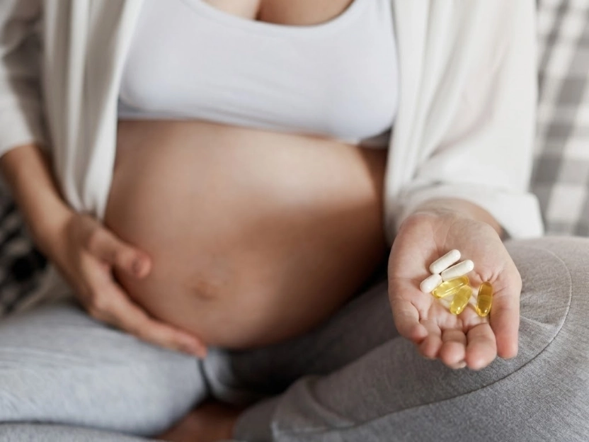  Close-up de uma mulher grávida sentada, com uma mão na barriga e a outra segurando cápsulas de suplementos, ilustrando a importância da suplementação na gravidez.