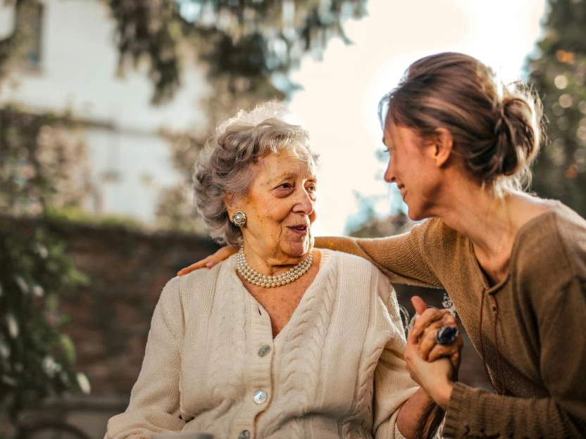 Mulher mais jovem sorrindo e conversando com uma mulher idosa em um ambiente externo