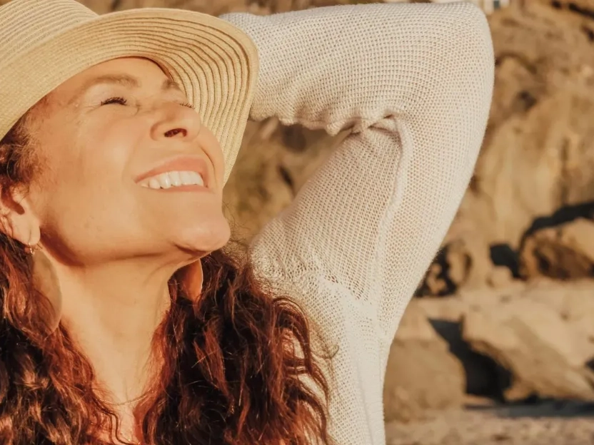 Uma mulher sorri com os olhos fechados enquanto a luz do sol ilumina seu rosto