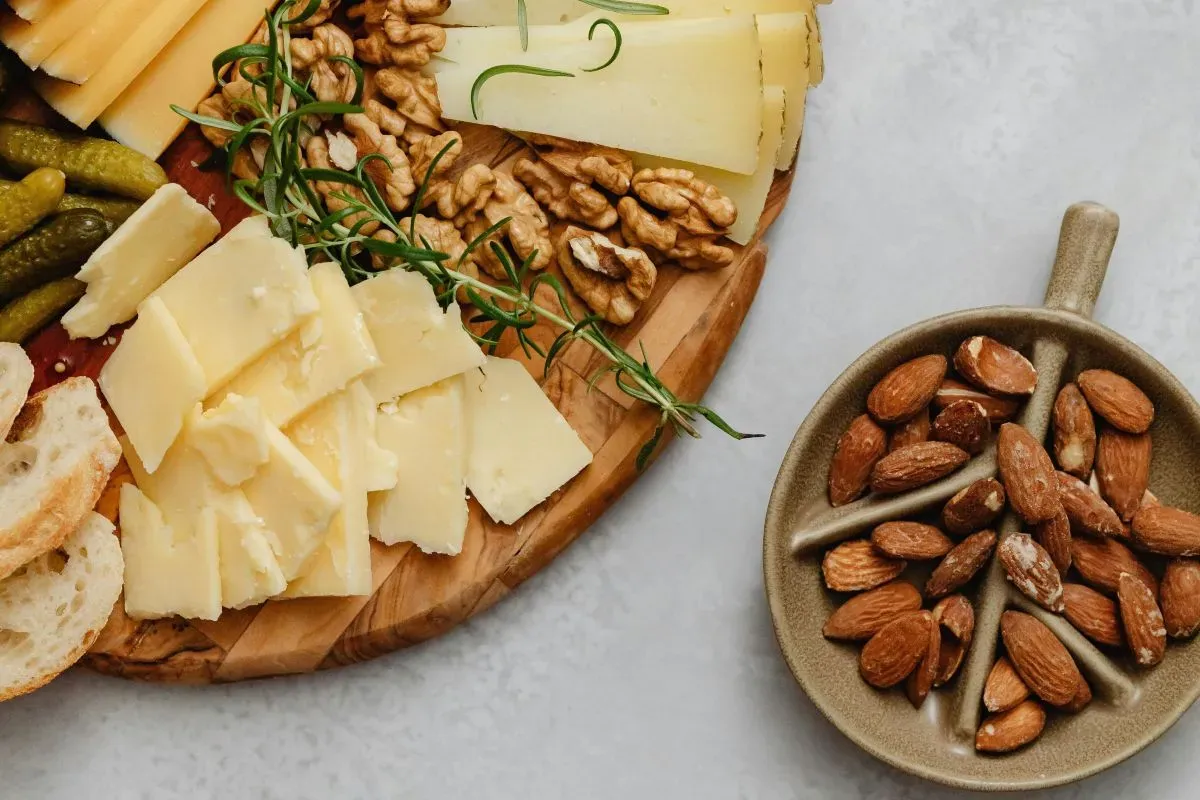 Uma tábua com diversos queijos, nozes e amêndoas, mostrando opções deliciosas e ricas em cálcio para compor uma alimentação saudável.